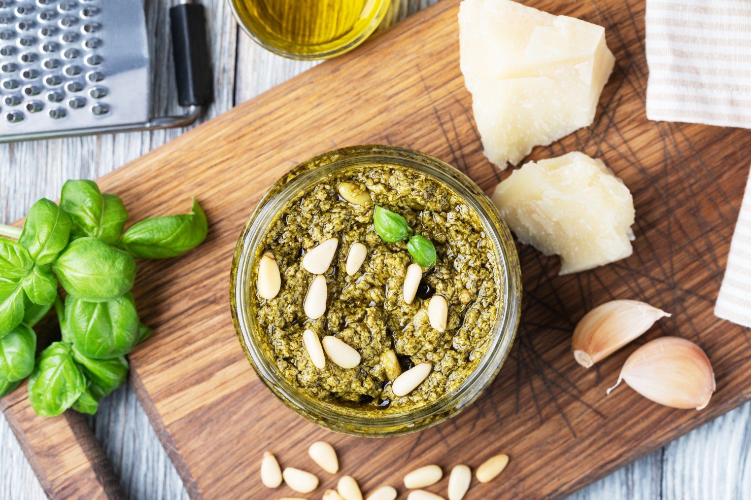 Alimentación con Semillas de Calabaza - Preparación de salsa pesto. Albahaca, aceite de oliva, parmesano, ajo y piñones. Aislado sobre fondo blanco.