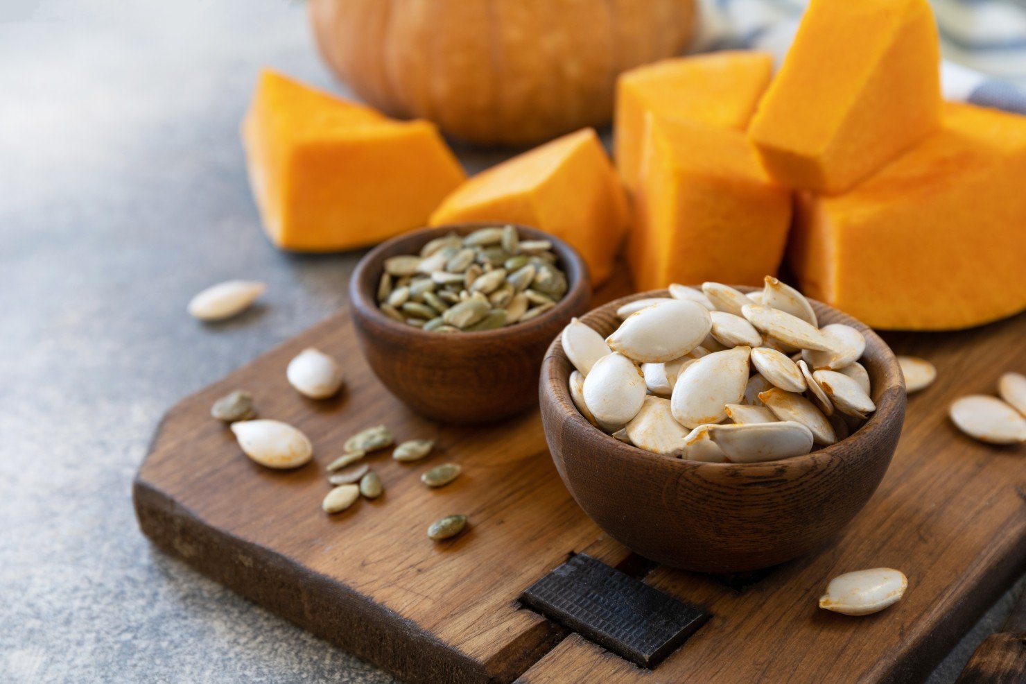 Alimentación con Semillas de Calabaza - Semillas de calabaza crudas, superalimentos, después de la cosecha. Semillas de calabaza en un tazón de madera sobre un fondo de piedra gris. Copiar espacio.