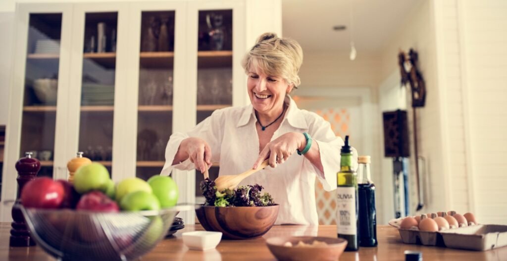 Mujer mayor con alimentos de dietas saludables cocinando en la cocina.